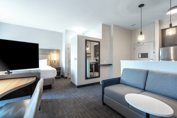 A modern hotel room with a flat-screen TV, a sofa, a small table, a bed, and a kitchenette area. - Residence Inn by Marriott Anderson Clemson (Anderson)