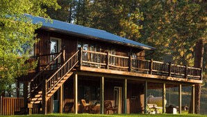A two-story wooden cabin with a balcony, outdoor seating, and a covered porch. - Stable View Cabin - Alpine Falls Ranch (Superior)