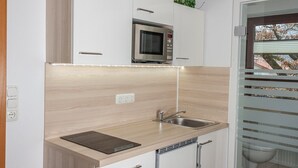 Een moderne keuken met witte kasten, een ingebouwde magnetron, een spoelbak en een raam met uitzicht op een tuin.