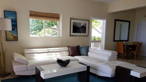 Ein Wohnzimmer mit weißem Sofa, einem Couchtisch und einem Essbereich mit Tisch und Stühlen.