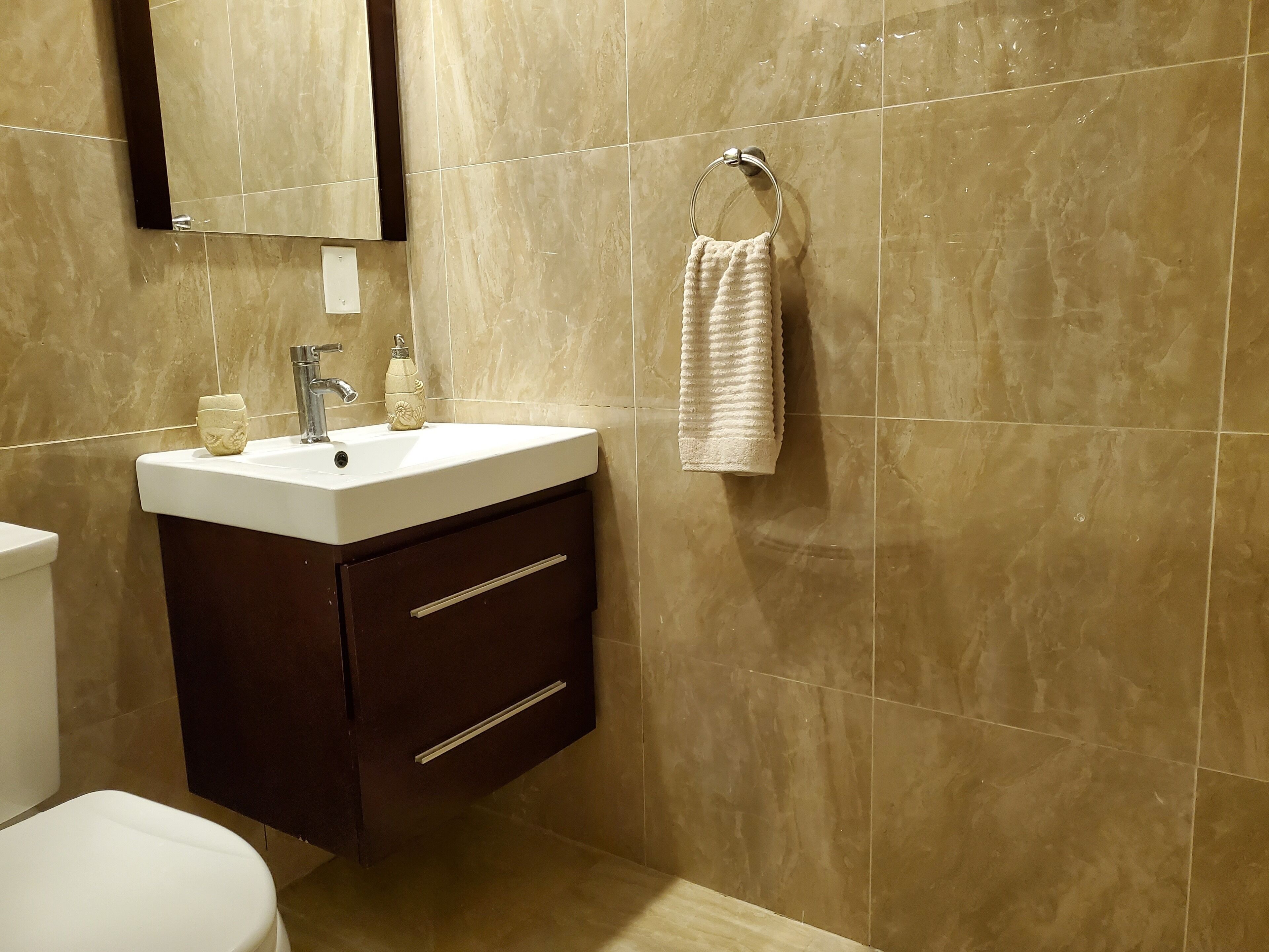 A bathroom with a white sink, dark cabinet, and a towel hanging on a ring.