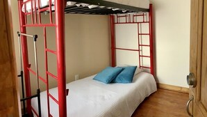 Un lit superposé avec une structure rouge, du linge de lit blanc et un oreiller bleu.
