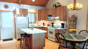 A kitchen with wooden cabinets, a central island, a dining table with chairs, a chandelier, and a refrigerator.