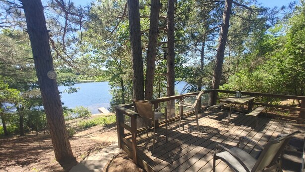 A wooden deck with outdoor seating overlooking a lake, surrounded by trees.