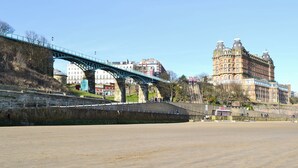 A coastal area with a bridge, a sandy beach, and historic buildings in the background. - Seaton Mote - UK31992 (Staithes)