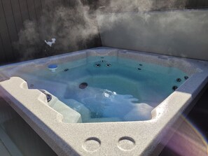 Un bain à remous avec une structure extérieure en pierre, des orifices d’évacuation apparents et un couvercle bleu.