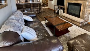 Ein modernes Wohnzimmer mit einer ledernen Eckcouch, einem Holztisch, einem Kamin und einer Küche im Hintergrund.