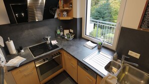 Una cocina moderna con estufa, horno, lavamanos y ventana con vista a árboles.