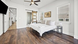 A bedroom with a large bed, a ceiling fan, a window with blinds, and a painting on the wall. - Modern Biz-Friendly Duplex mins to DT/Convention Center W/Ping Pong & More! (Dallas)