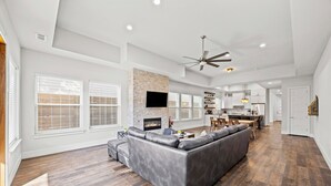 A spacious living room with a large gray sectional sofa, a fireplace, and a dining area with a kitchen in the background. - Modern Biz-Friendly Duplex mins to DT/Convention Center W/Ping Pong & More! (Dallas)