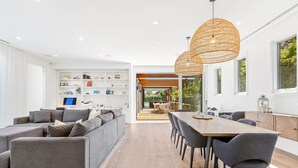 A modern living room with a grey sectional sofa, a wooden dining table with chairs, and a bookshelf filled with books and decorative items. - Resort style home, Pool & Tennis court, walk to Beach & Village (sleeps 10) (Blairgowrie)