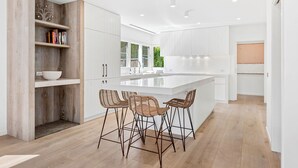 A modern kitchen with a large island, bar stools, and wooden shelves. - Resort style home, Pool & Tennis court, walk to Beach & Village (sleeps 10) (Blairgowrie)