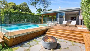 A modern outdoor pool area with a wooden deck, a fire pit, and outdoor seating. - Resort style home, Pool & Tennis court, walk to Beach & Village (sleeps 10) (Blairgowrie)