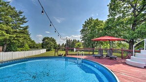 Ein Schwimmbecken mit Holzterrasse, einem roten Sonnenschirm und Lichterketten.