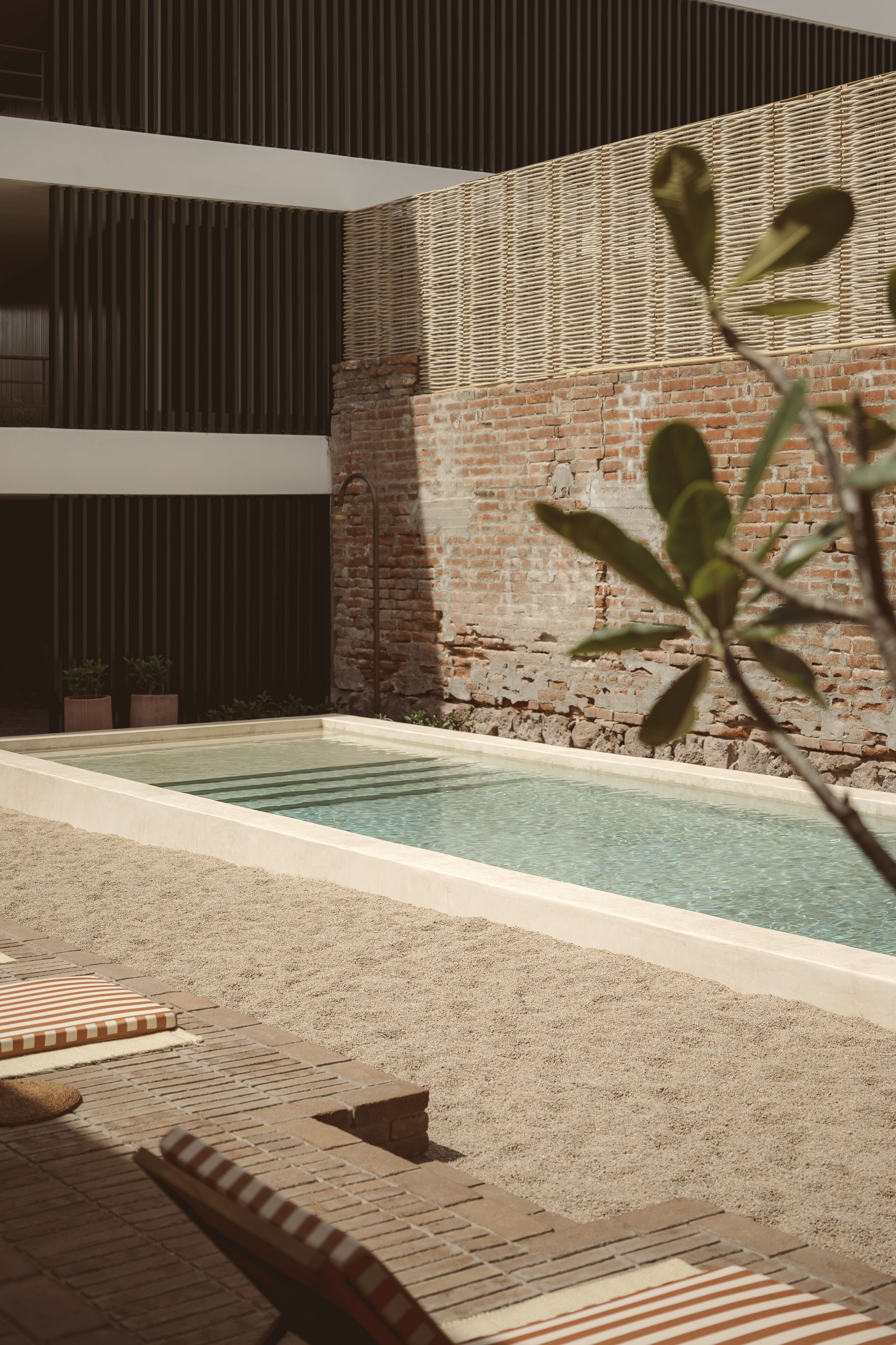 A pool area with a brick wall, lounge chairs, and potted plants.