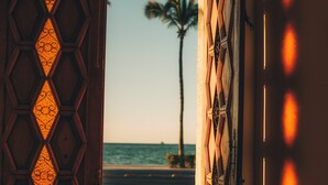 A wooden door with a geometric pattern, leading to a beach with a palm tree and the ocean in the background. - Baja Club Hotel, La Paz, Baja California Sur, a Member of Design Hotels (La Paz)
