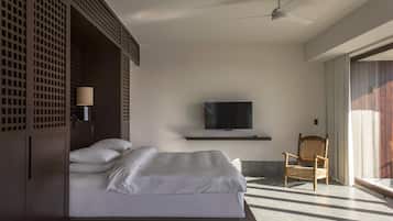 Una habitación de hotel moderna con una cama grande, un televisor montado en la pared, una silla y un ventilador de techo.