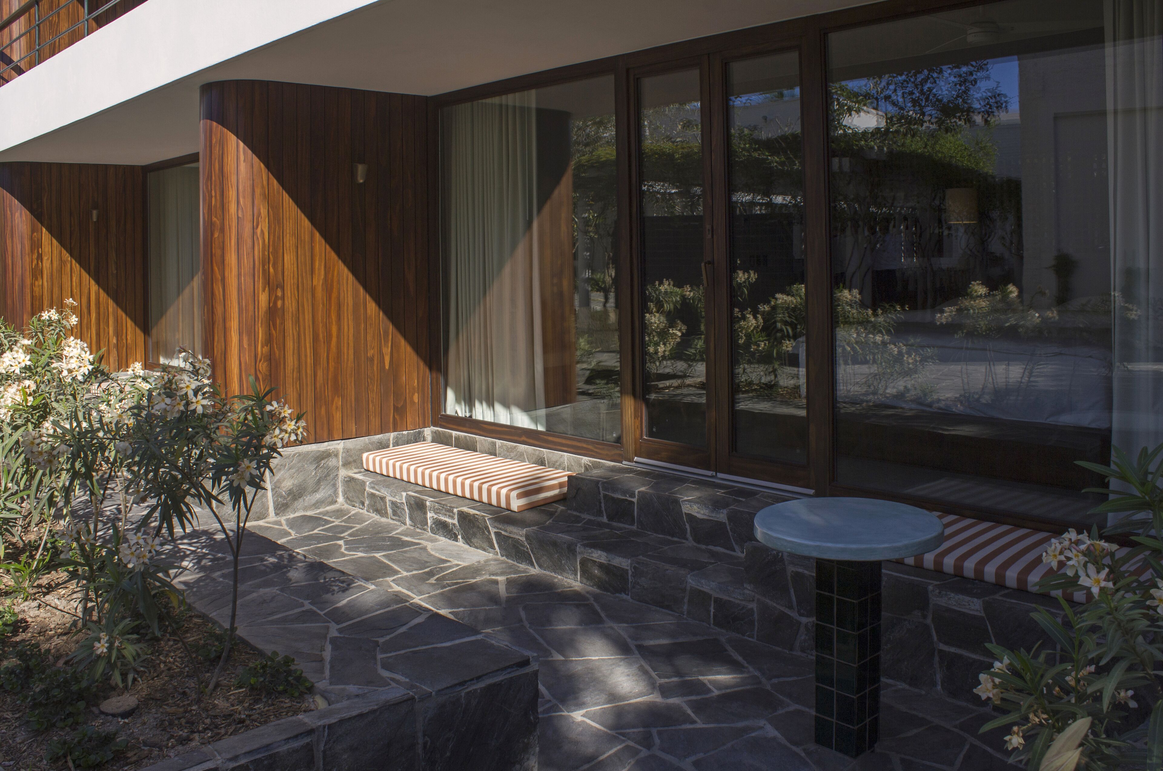 Un patio moderno al aire libre con piso de piedra, detalles de madera y un área de estar con cojines.