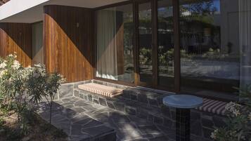 Un patio moderno al aire libre con piso de piedra, detalles de madera y un área de estar con cojines.
