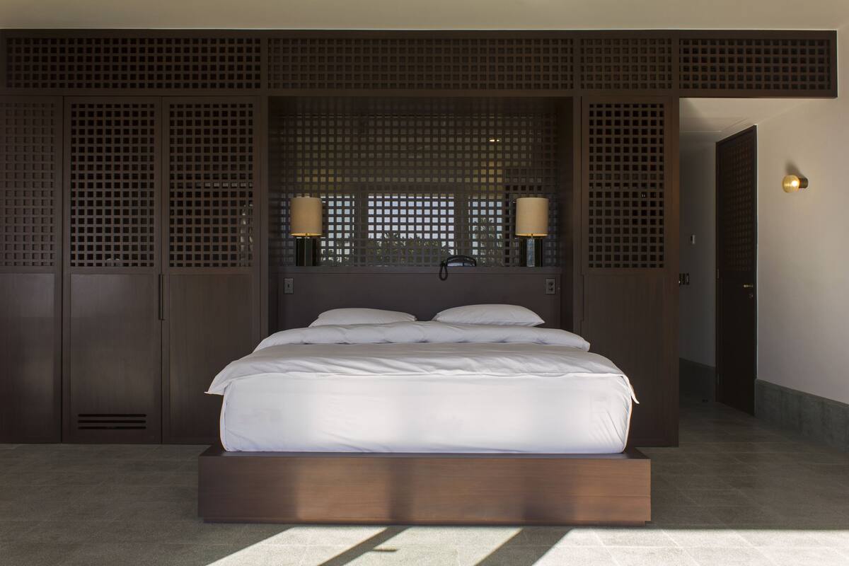 A modern hotel room with a large bed, wooden headboard, and two bedside lamps.