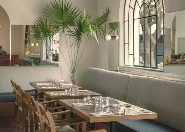 A restaurant with wooden tables and chairs, a cushioned bench, and large windows with natural light. - Baja Club Hotel, La Paz, Baja California Sur, a Member of Design Hotels (La Paz)