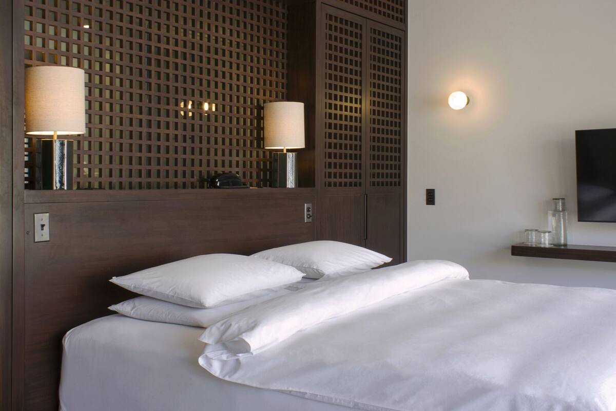 A hotel room with a large bed, two bedside lamps, a ceiling fan, and a TV on the wall.