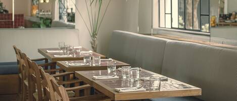 L’intérieur d’un restaurant est agrémenté de tables en bois, de bancs rembourrés et de grands pots de plantes.
