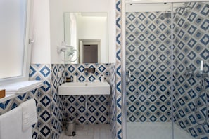 Un baño con un lavamanos blanco, un espejo encima y una zona de ducha con un muro de azulejos estampados.
