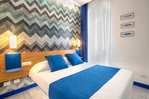 A hotel room with a bed, blue bedding, a chevron-patterned wall, and framed fish artwork. - Bright&Modern Suite in Sorrento Old Town (Sorrento)