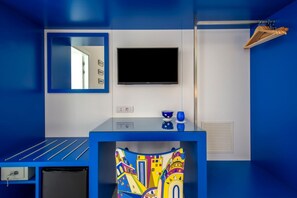 Une salle de bain moderne aux tons bleus, avec un miroir, un téléviseur à écran plat, un lavabo agrémenté d’une serviette colorée et un porte-serviettes.
