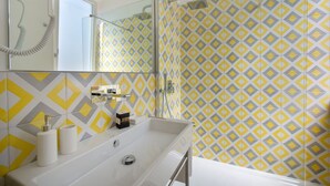 Ein Badezimmer mit weißem Waschbecken, Spiegel und Dusche. Die Wände sind mit einem geometrischen Muster aus gelben und grauen Fliesen versehen.
