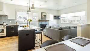 A modern kitchen with a central island, a dining area with a table and chairs, a gray sofa, and a fireplace. - Cute COTTAGE for family fun ~ hot tub + firepit ~ near park ~ resort pool ~ BEND (Bend)