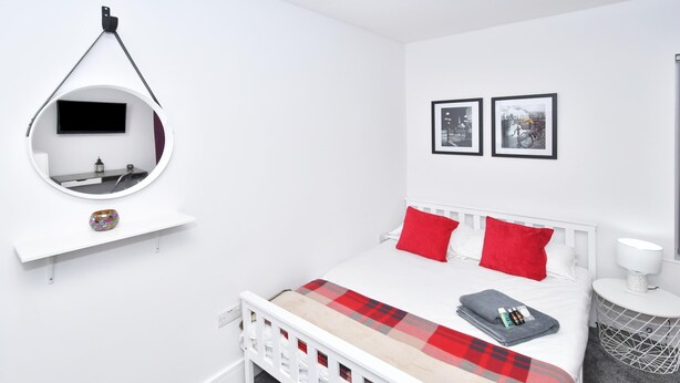Ein Schlafzimmer mit einem Bett, einem runden Spiegel, einem Fernseher, zwei gerahmten Bildern und einem Nachttisch mit einer Lampe.