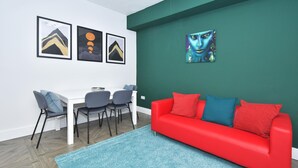 A modern living room with a red sofa, blue and red cushions, a white dining table with four chairs, and three framed artworks on the wall. - Townhouse @ 42 Minshull New Road Crewe (Crewe)