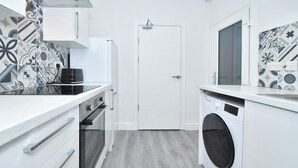A modern kitchen with white cabinetry, a built-in oven, a washing machine, and patterned backsplash tiles. - Townhouse @ 42 Minshull New Road Crewe (Crewe)