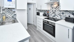 A modern kitchen with white cabinets, a built-in microwave, a stove, and a sink. - Townhouse @ 42 Minshull New Road Crewe (Crewe)