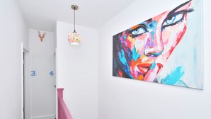 A hallway with a colorful abstract painting, a decorative ceiling light, and a pink railing. - Townhouse @ 42 Minshull New Road Crewe (Crewe)