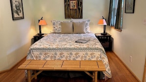 A neatly arranged bedroom with a bed, two bedside tables, a bedside lamp, a wooden bench, and framed artwork on the walls.