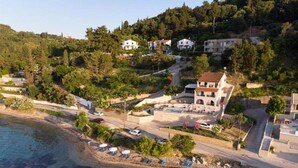 Ein Küsteneigentum mit Swimmingpool, Liegestühlen am Strand und einer Anhöhe mit Wohnhäusern.