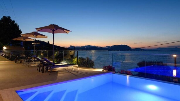 Ein Poolbereich auf dem Dach mit Liegestühlen und Sonnenschirmen mit Blick auf ein Gewässer im Abenddämmerung.
