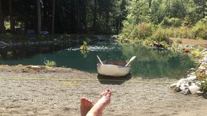 A serene outdoor setting with a pond, a small boat, and a sandy area. - Hidden Pond Gong Suite - Luxury , Pet Friendly, with Hot Tub and Private Beach  (Victoria)