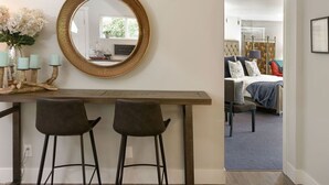 A room with a round mirror on the wall, a wooden table with two chairs, and a view into a bedroom with a bed and a chair. - Hidden Pond Gong Suite - Luxury , Pet Friendly, with Hot Tub and Private Beach  (Victoria)