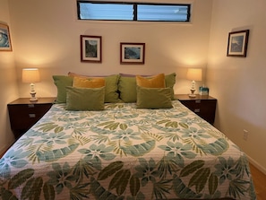 Une chambre à coucher avec un lit, deux tables de chevet, deux lampes et trois tableaux encadrés accrochés au mur.