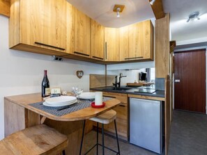 A compact kitchen with wooden cabinets, a small refrigerator, and a bar stool.