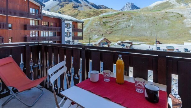 A balcony with a red table, a bottle, glasses, and a chair. - Rond Point des Pistes (Val Claret) by Interhome (Tignes)