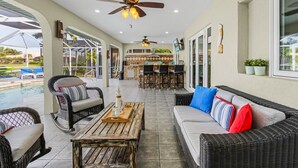 A spacious patio area with wicker furniture, a pool, and a bar area. - Private Beach, Heated Pool, Kayaks, & Pool Table - Villa Las Palmas - Roelens Vacations (Cape Coral)