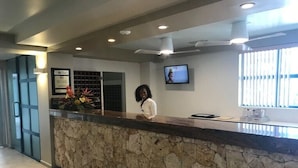 A reception area with a stone counter, a television mounted on the wall, and a window providing natural light. - Maho Royal Islander, La Terrasse 2br 2ba Beautiful White Sand Beach (Lowlands)