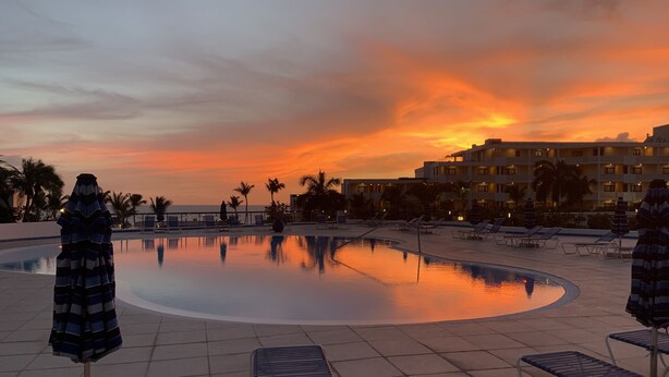 A swimming pool with lounge chairs and umbrellas, surrounded by palm trees and a hotel building. - Maho Royal Islander, La Terrasse 2br 2ba Beautiful White Sand Beach (Lowlands)