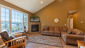 A living room with a fireplace, large windows, a ceiling fan, and a view of the outdoors. - Private pool, boat rental, hiking and enjoying all the great restaurants in the area. (Lake Ozark)