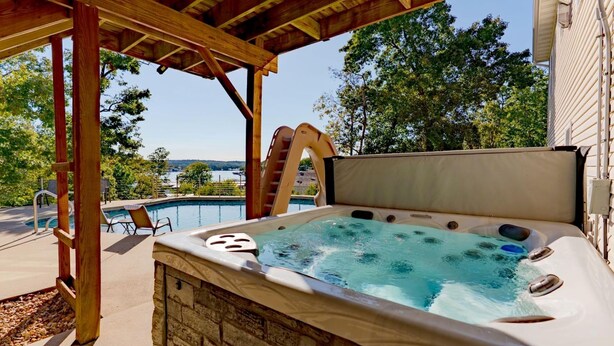 A hot tub with a view of a swimming pool and trees. - Private pool, boat rental, hiking and enjoying all the great restaurants in the area. (Lake Ozark)